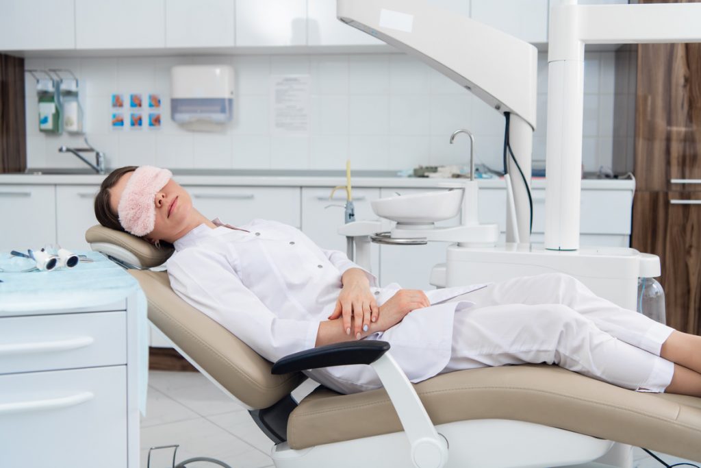 A woman in a dentists chair with a sleep mask on.