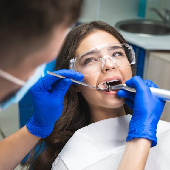 Dentist examining a smiling young woman's teeth with a dental mirror and tool