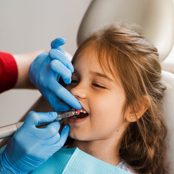 Child dentist makes professional teeth cleaning in dentistry. Professional hygiene for teeth of child in dentistry. Pediatric dentist examines and consults kid patient in dentistry